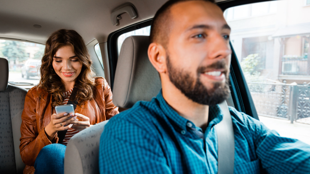 Man driving a woman who's looking at her cell phone.