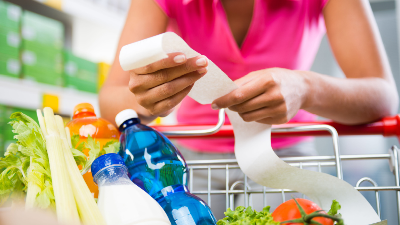 Woman reviewing receipt with a cart full of groceries.