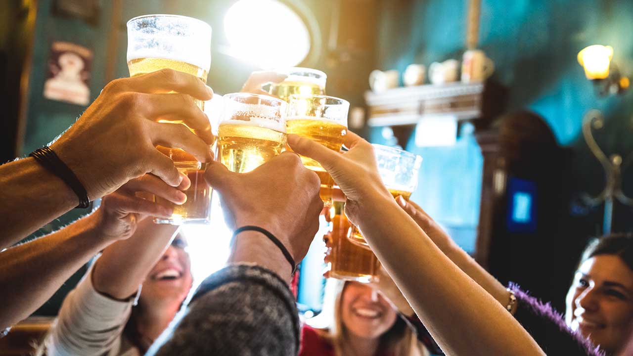 Group of happy friends drinking and toasting beer at brewery bar restaurant - Friendship concept with young people having fun together at cool vintage pub - Focus on middle pint glass.
