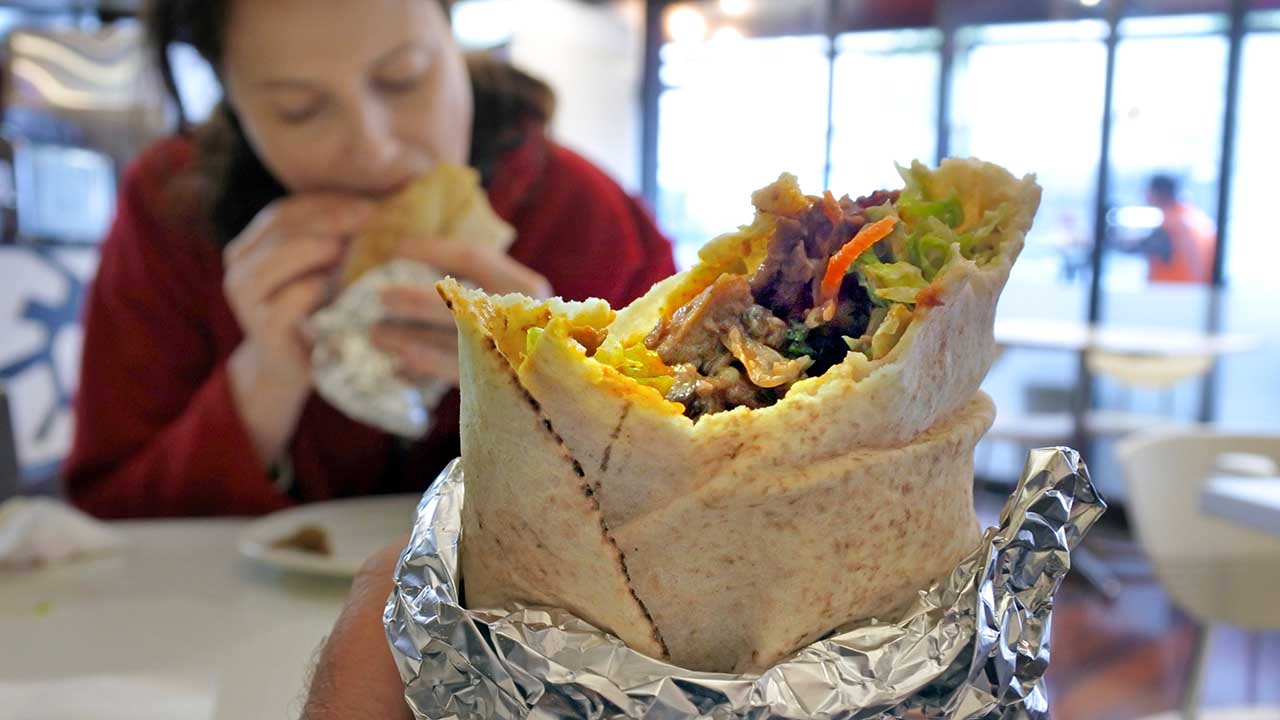 Close up of person eats Kebab wrap with grilled lamb and vegetables outdoors in city street. Lunch Time.