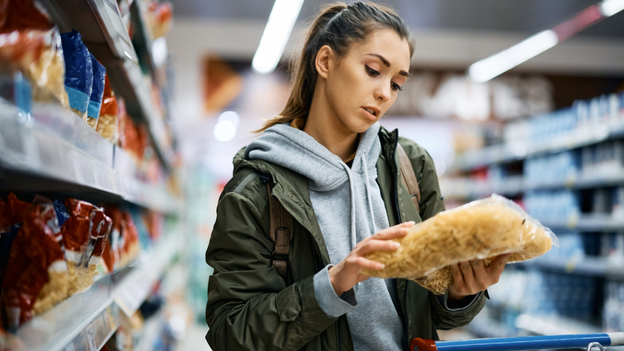 Young woman checking price while buying pasta at supermarket.