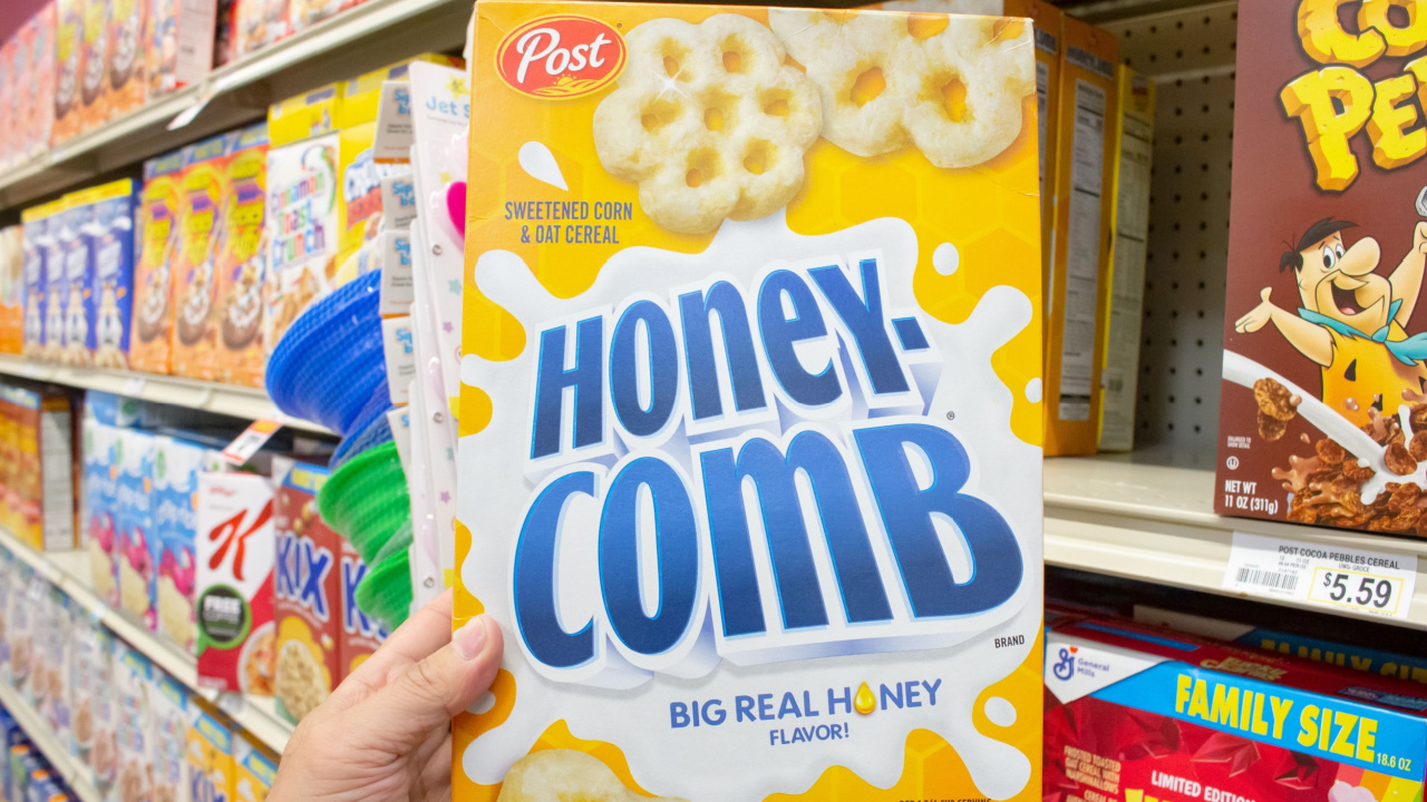 A view of a hand holding a package of Post Honeycomb cereal, on display at a local grocery store.