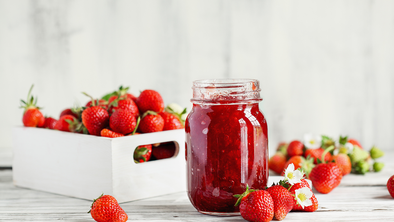Homemade strawberry preserves or jam in a mason jar surrounded by fresh organic strawberries. Selective focus with blurred foreground and background.