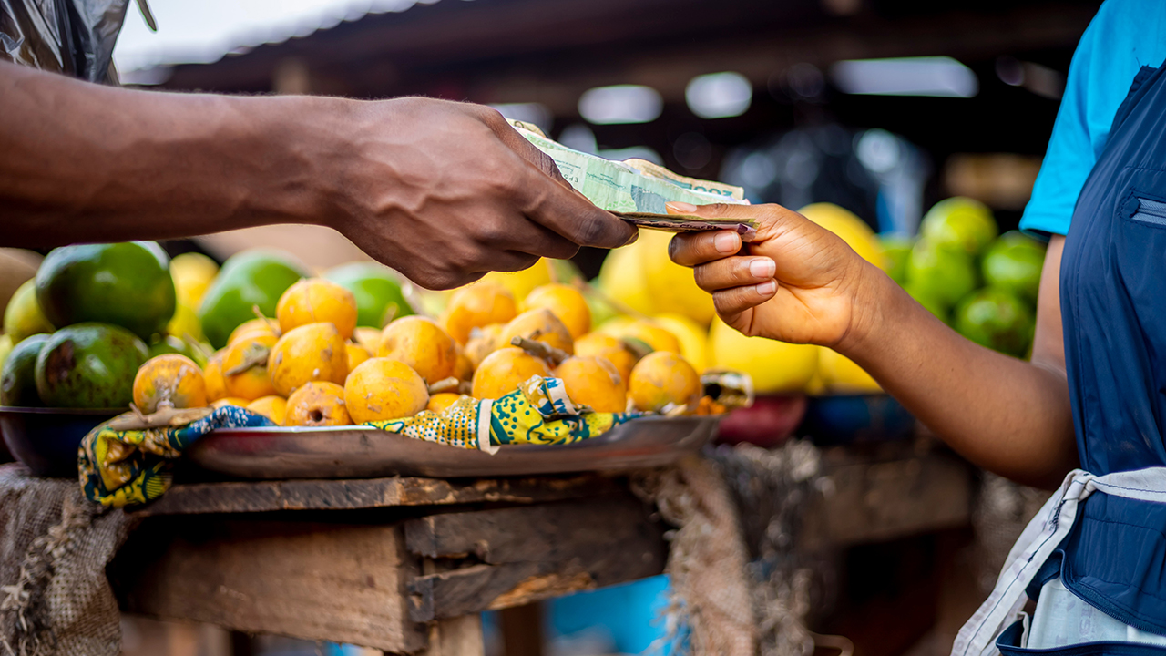 hands holding nigeria money near a fruit market. man paying for grocery in a local african market