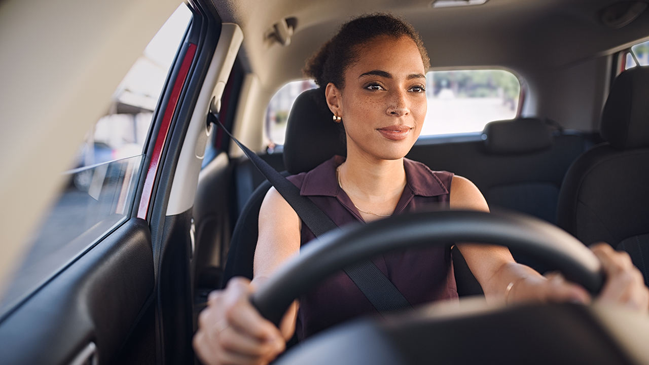 Smiling business woman driving car in city streets. Happy african american woman feeling comfortable sitting on driver seat in her new car. Mixed race girl with seat belt driving vehicle.