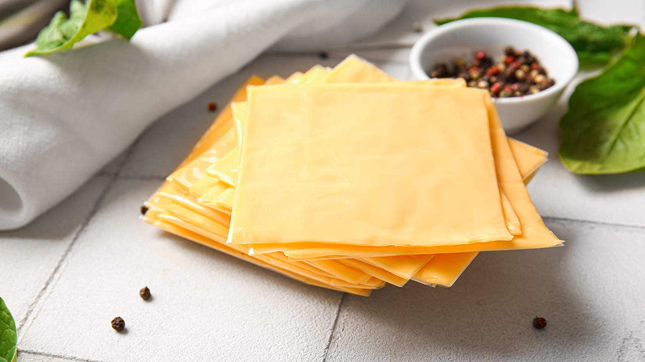 Slices of tasty processed cheese on white tile background